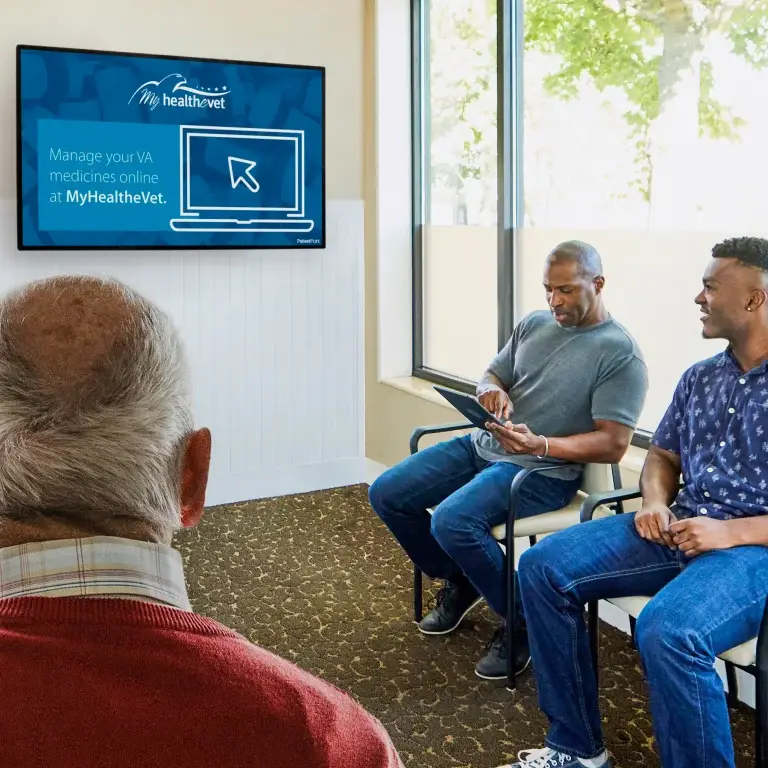 3 men view waiting room screen education about My HealtheVet message and managing VA prescriptions online.